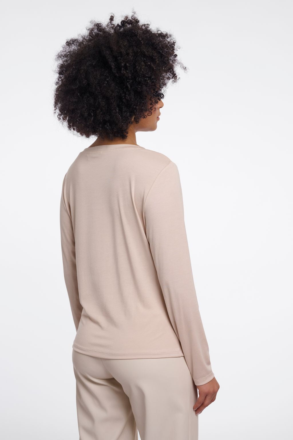 Woman wearing a beige long-sleeve crew neck top. 