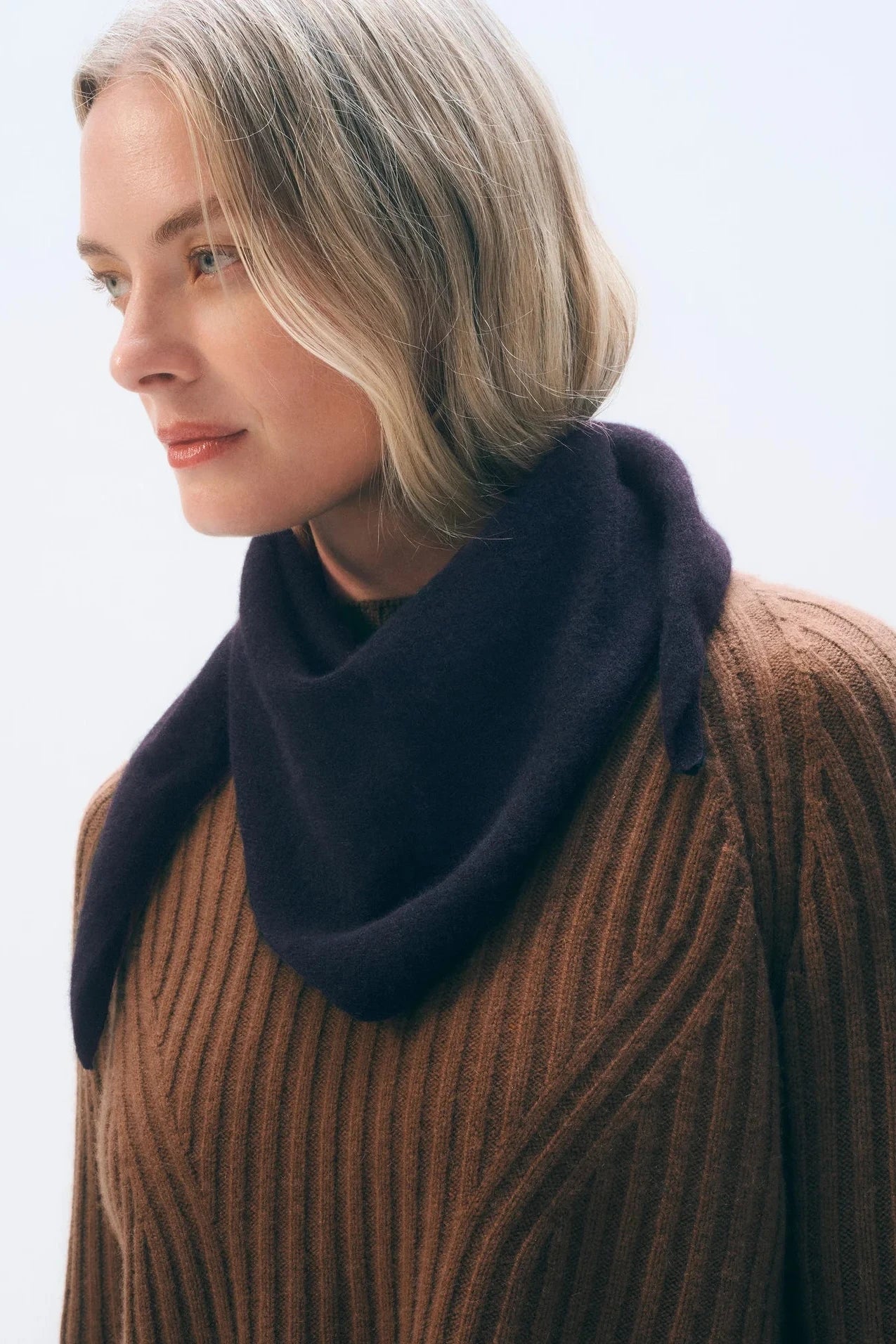 Woman wearing a brown sweater and dark purple scarf against a light background