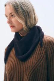 Woman wearing a brown sweater and dark purple scarf against a light background
