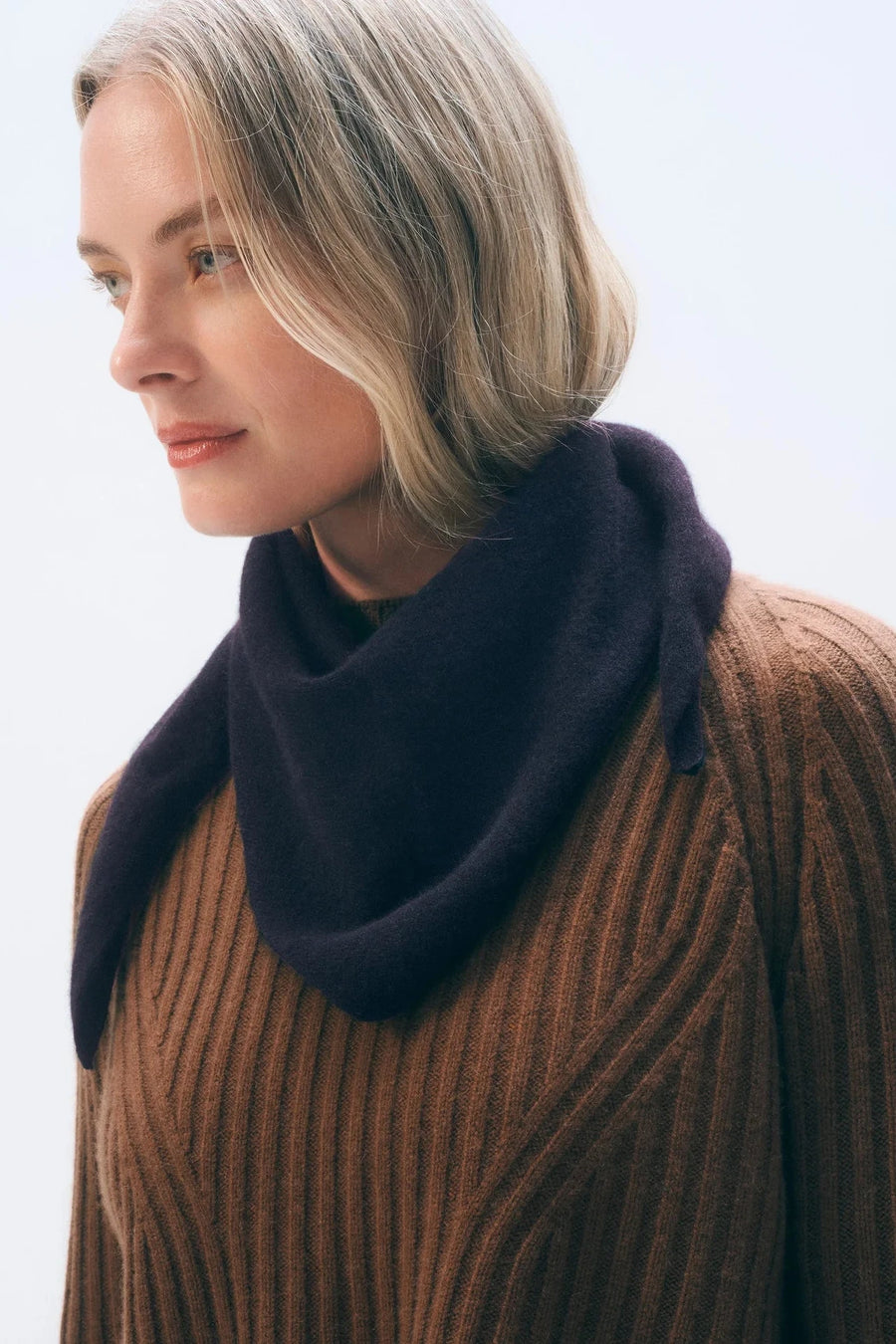 Woman wearing a brown sweater and dark purple scarf against a light background
