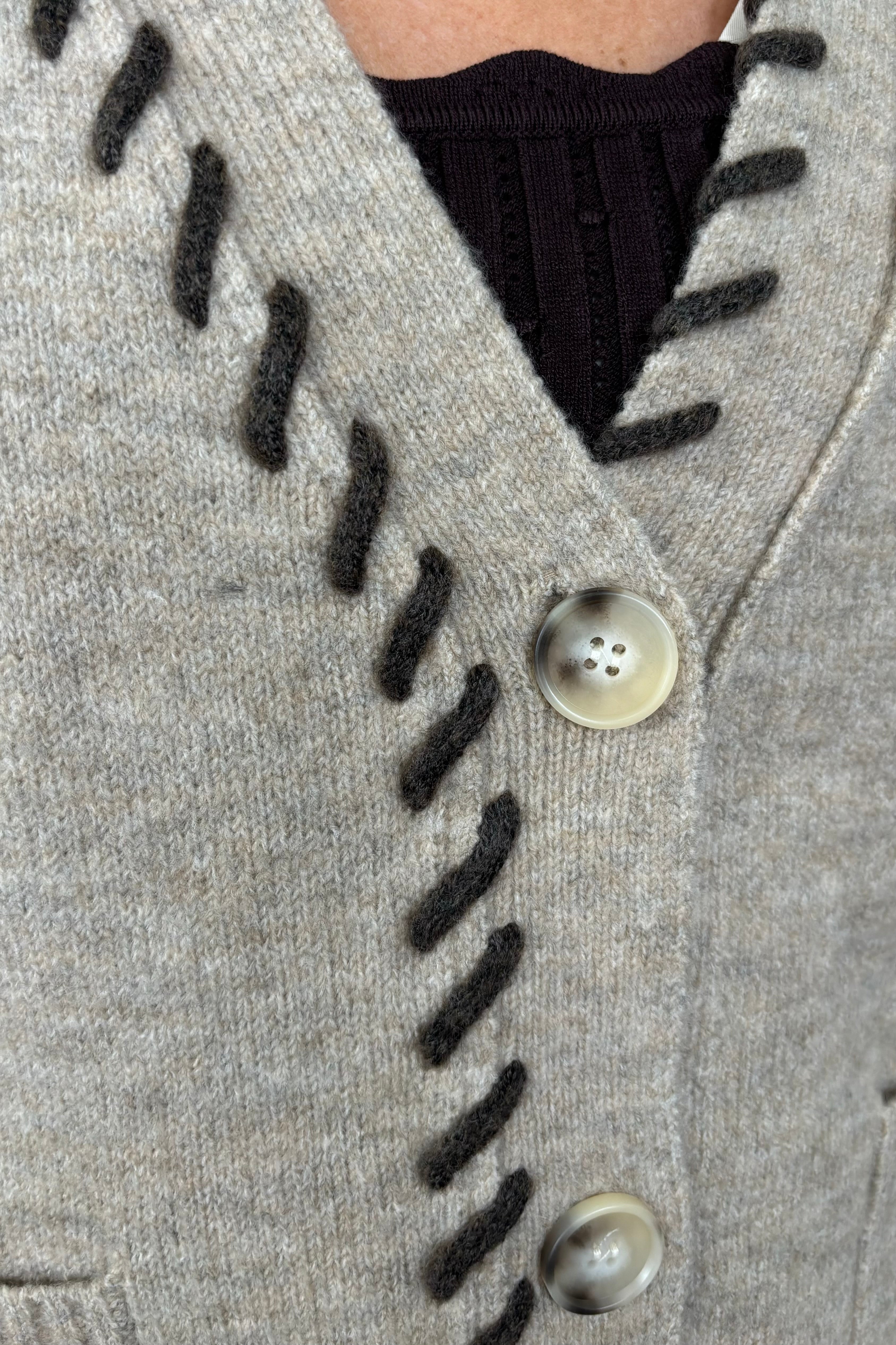 zoom in view of woman wearing a beige cardigan, v-neck and brown detailing