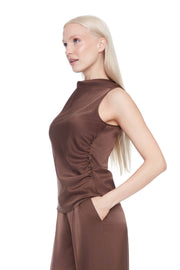 Woman wearing a satin brown sleeveless top and pants on a white 