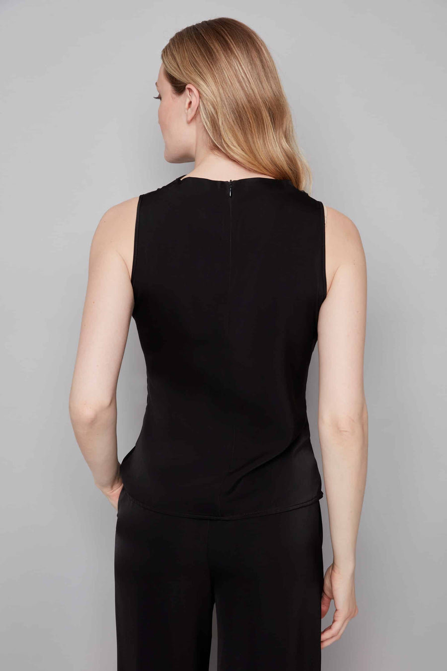 Woman wearing a black sleeveless top and black pants against a gray background