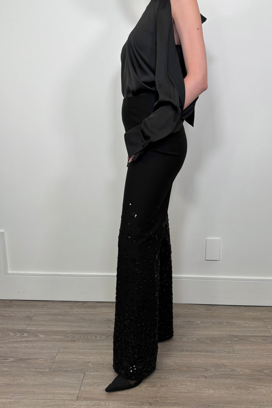 Person wearing a black outfit with sequin pants against a white wall.