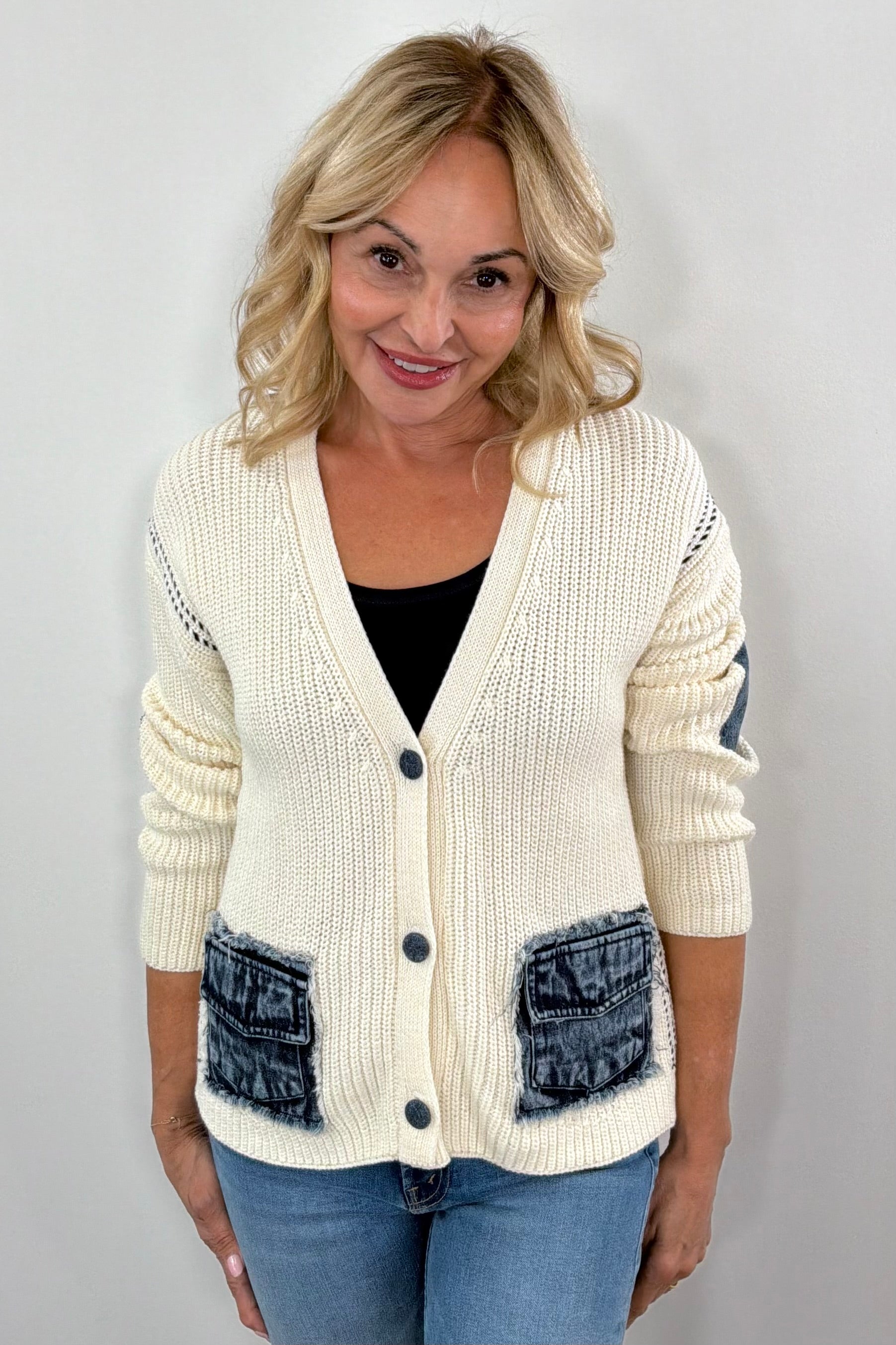Woman wearing a cream knit cardigan with denim pocket detail