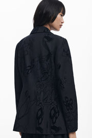 Back view of woman wearing a black blazer with textures flowers detailing