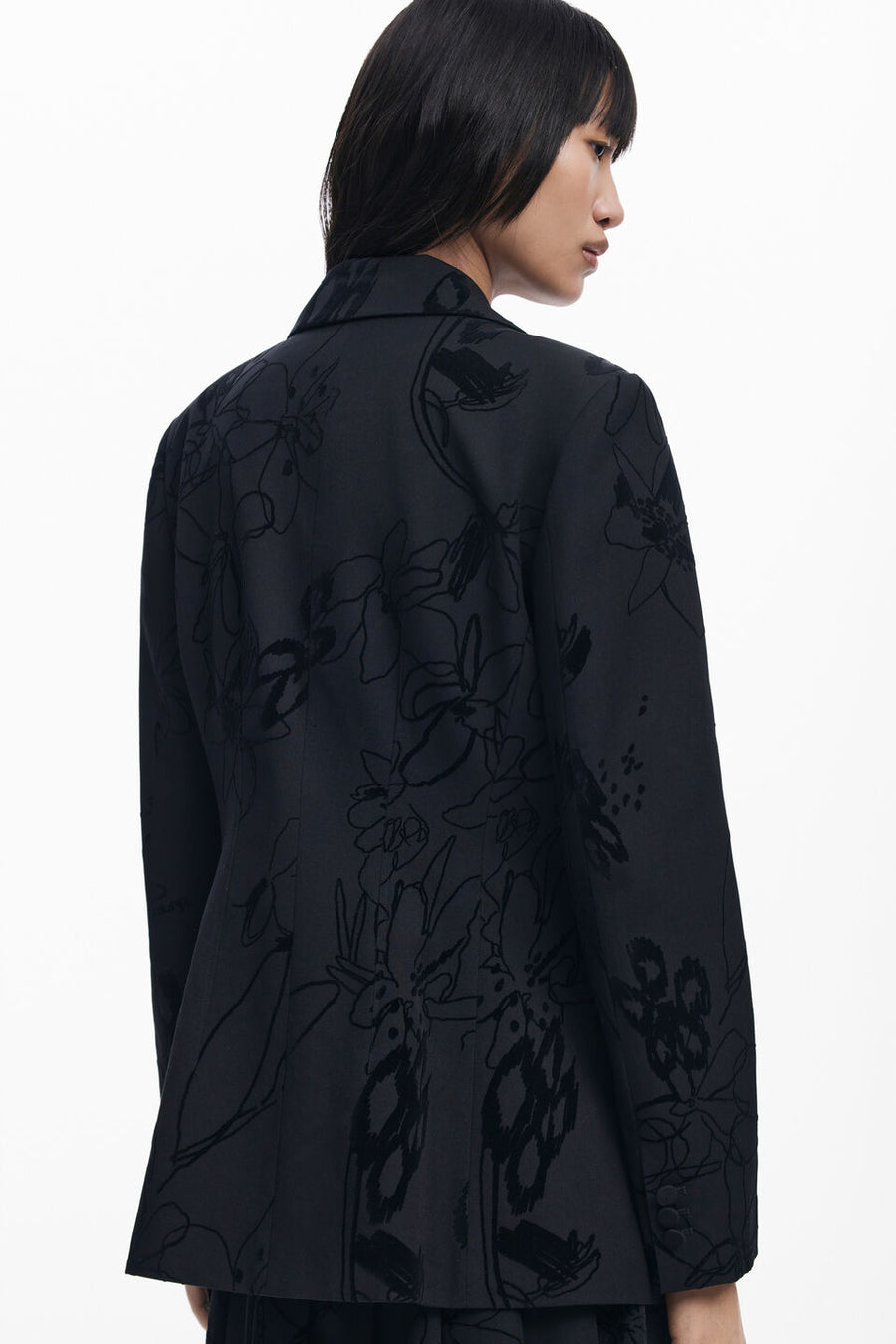 Back view of woman wearing a black blazer with textures flowers detailing