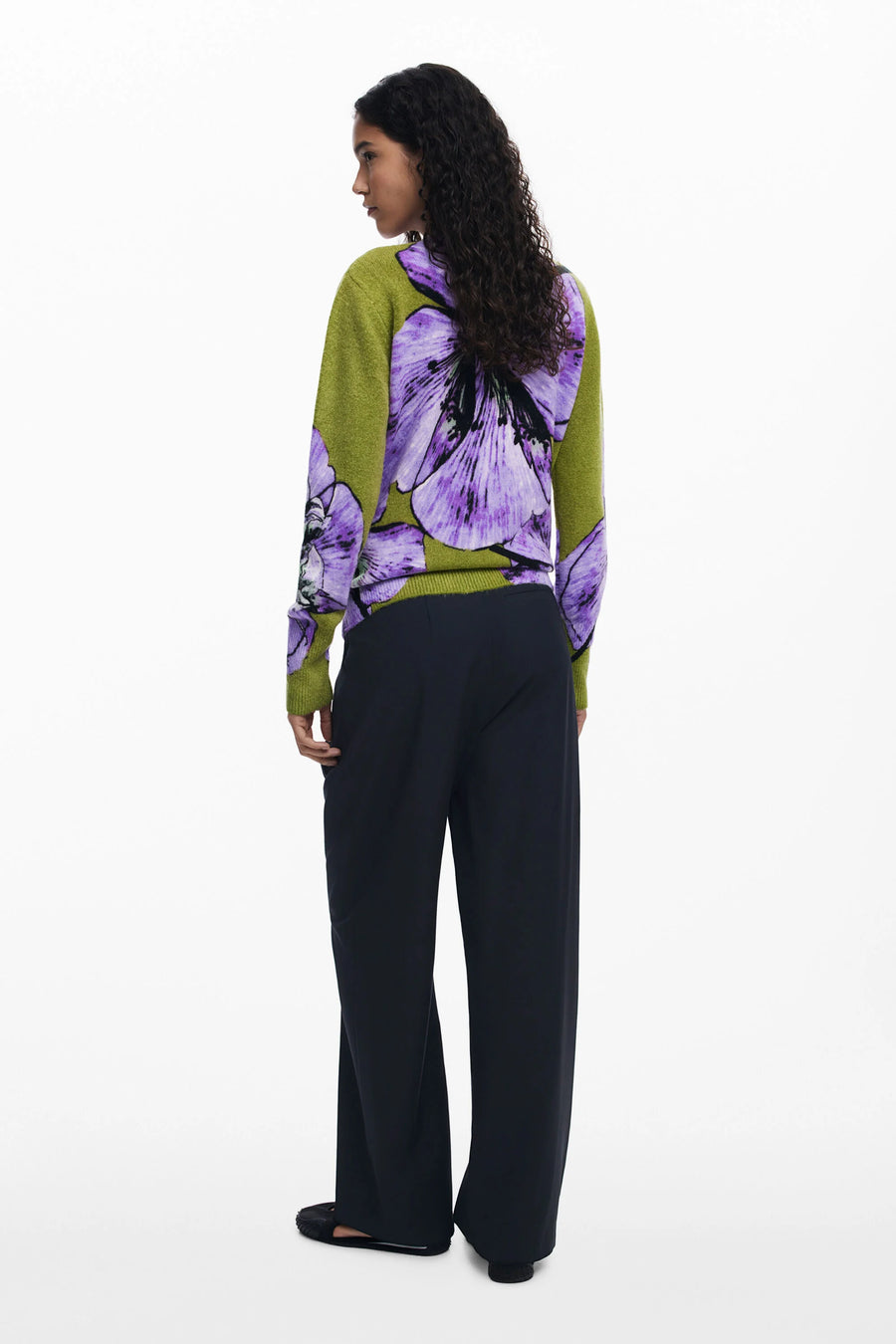 Woman wearing a green and purple floral blouse with black pants on a white background
