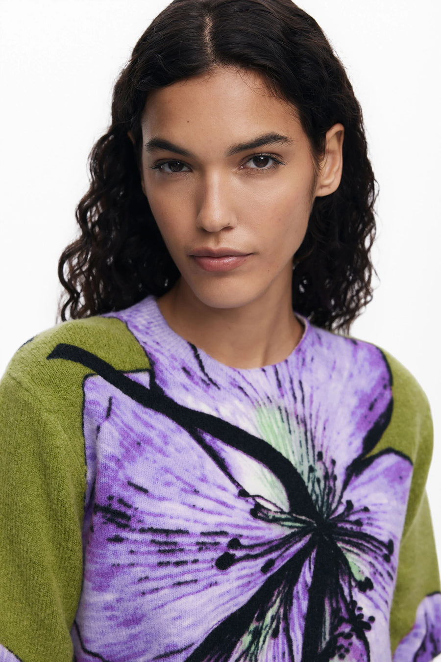 Woman wearing a green sweater with a purple floral design on a white background