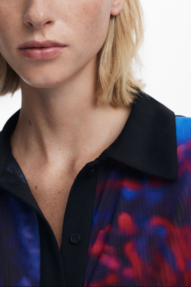 Cloe-up view of woman wearing a mesh button down shirt with blue and red patterns.