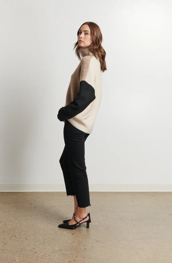 Woman wearing a two-tone sweater and black pants against a white background
