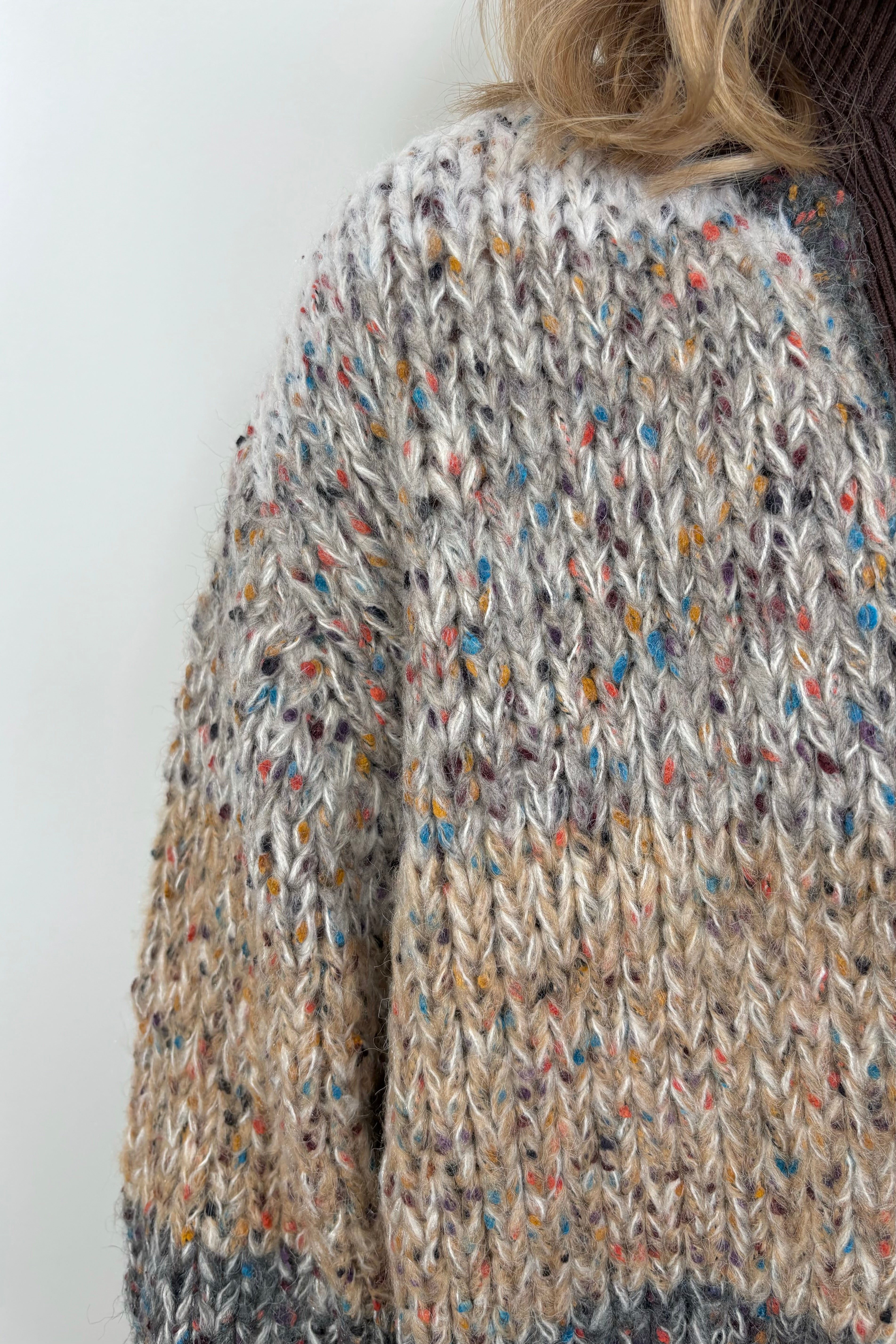Close up of woman wearing a light gray, beige and dark gray knitted cardigan
