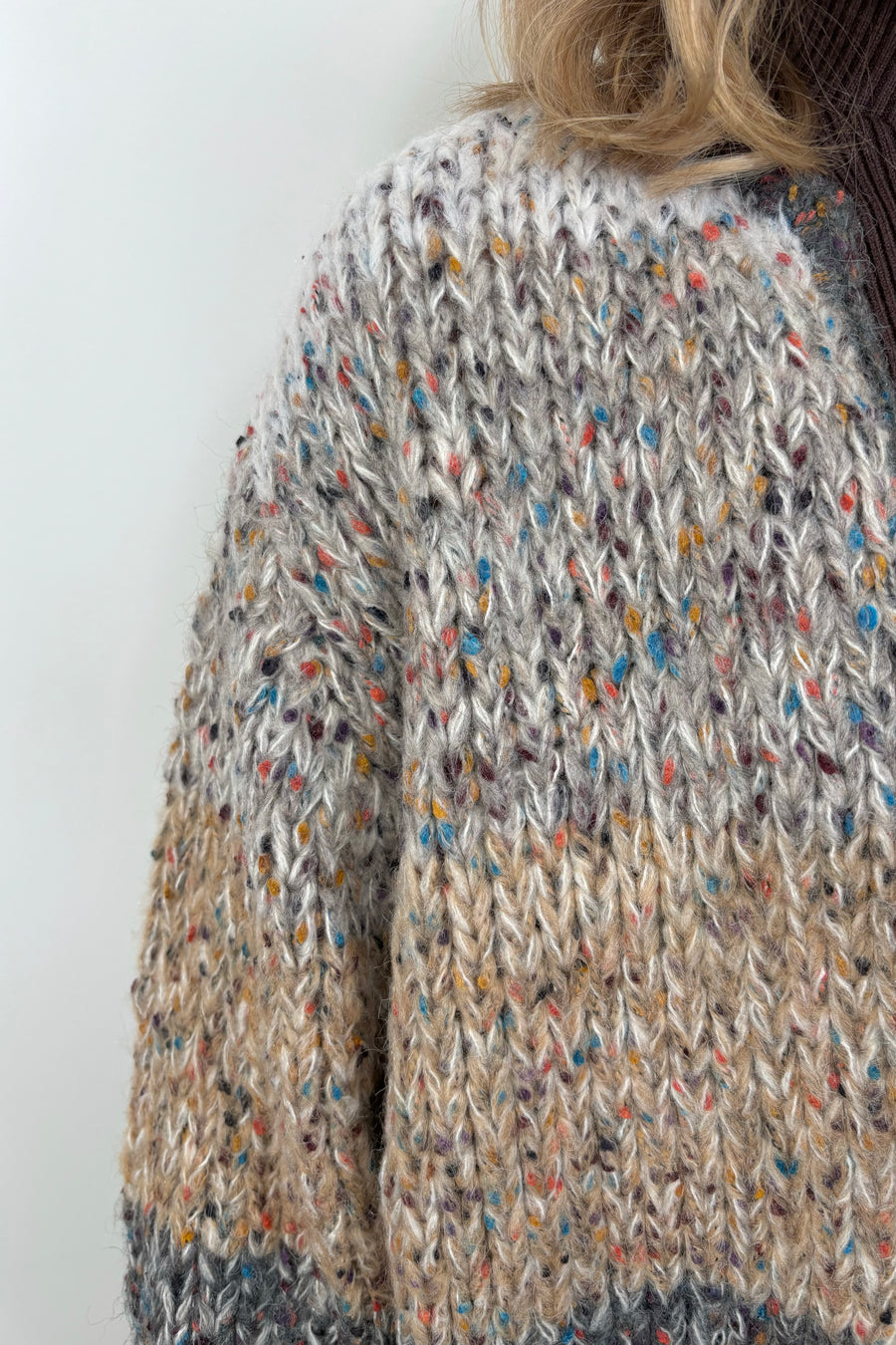 Close up of woman wearing a light gray, beige and dark gray knitted cardigan