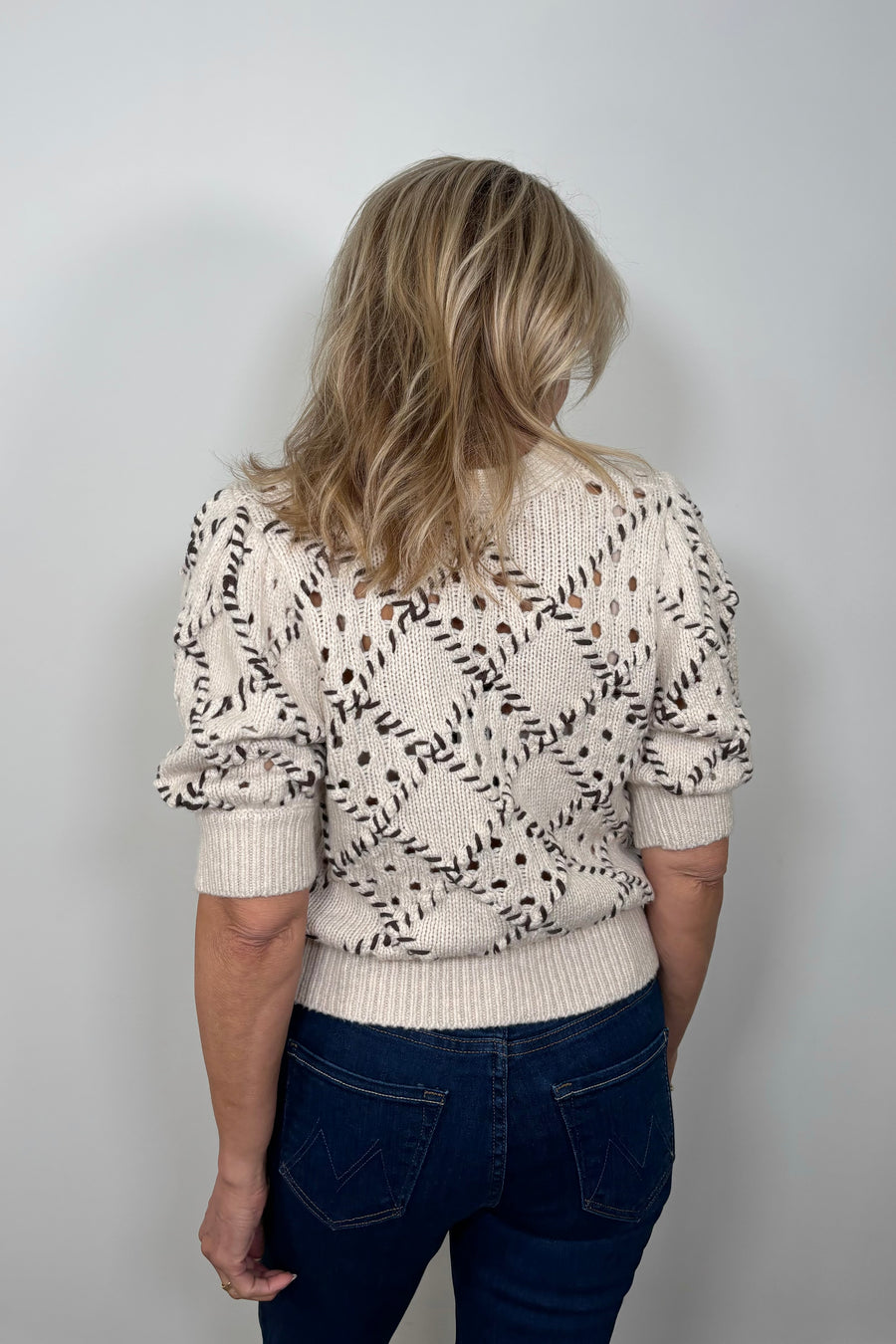Back view of a woman wearing a white knit cardigan with whipstitch detailing 