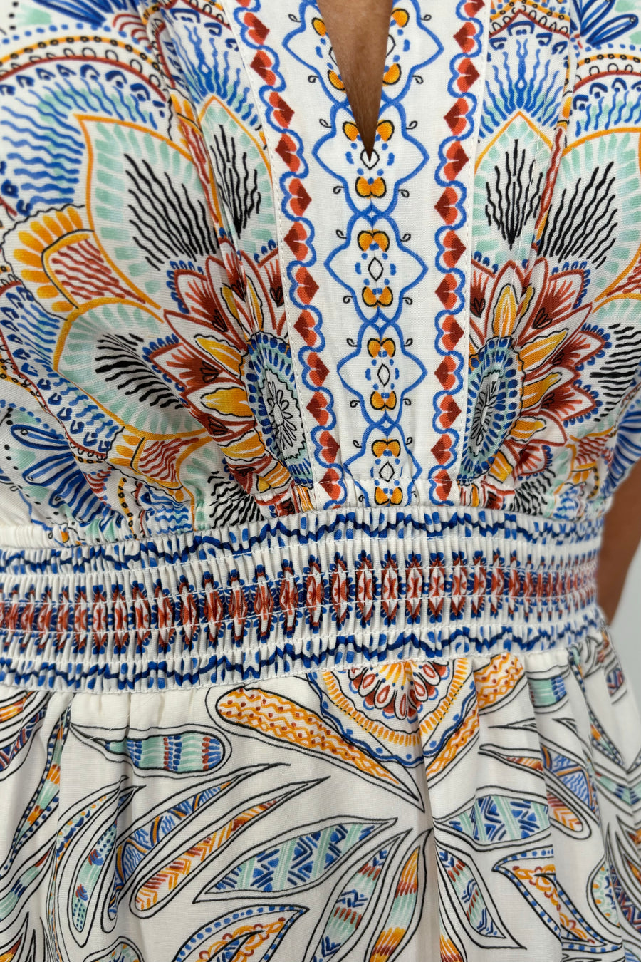 zoom into the neckline of a woman wearing white sleeveless midi dress with a blue, red and orange pattern