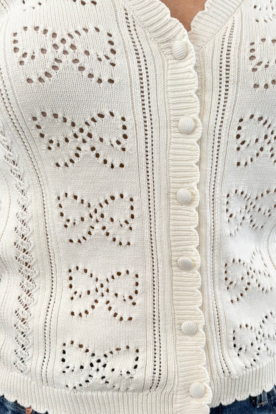 Close up of Woman wearing a cream cardigan with buttons on the front, scalloped trim and openwork detailing, front view
