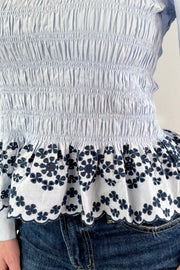 Close up of Woman wearing light blue smocked blouse with black detail