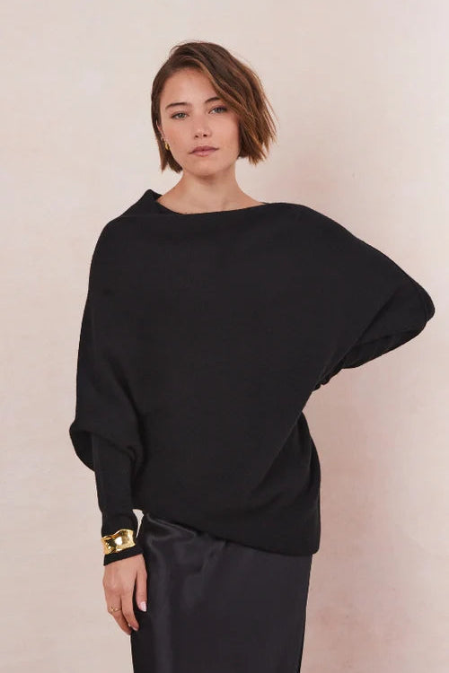 Person wearing a black sweater and black dress against a beige background