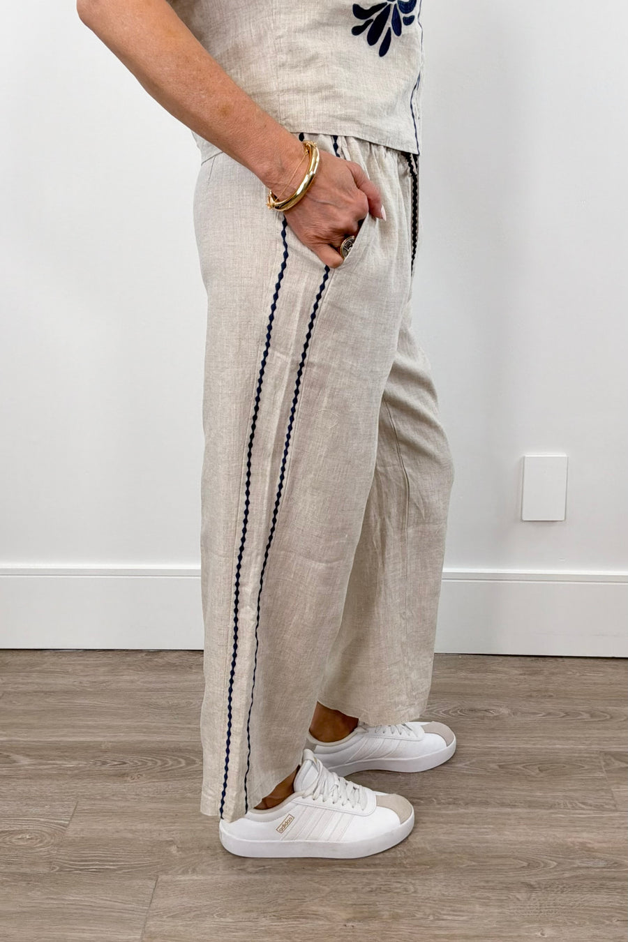 Woman wearing cream linen drawstring pants with contrast embroidery along the sides, side view