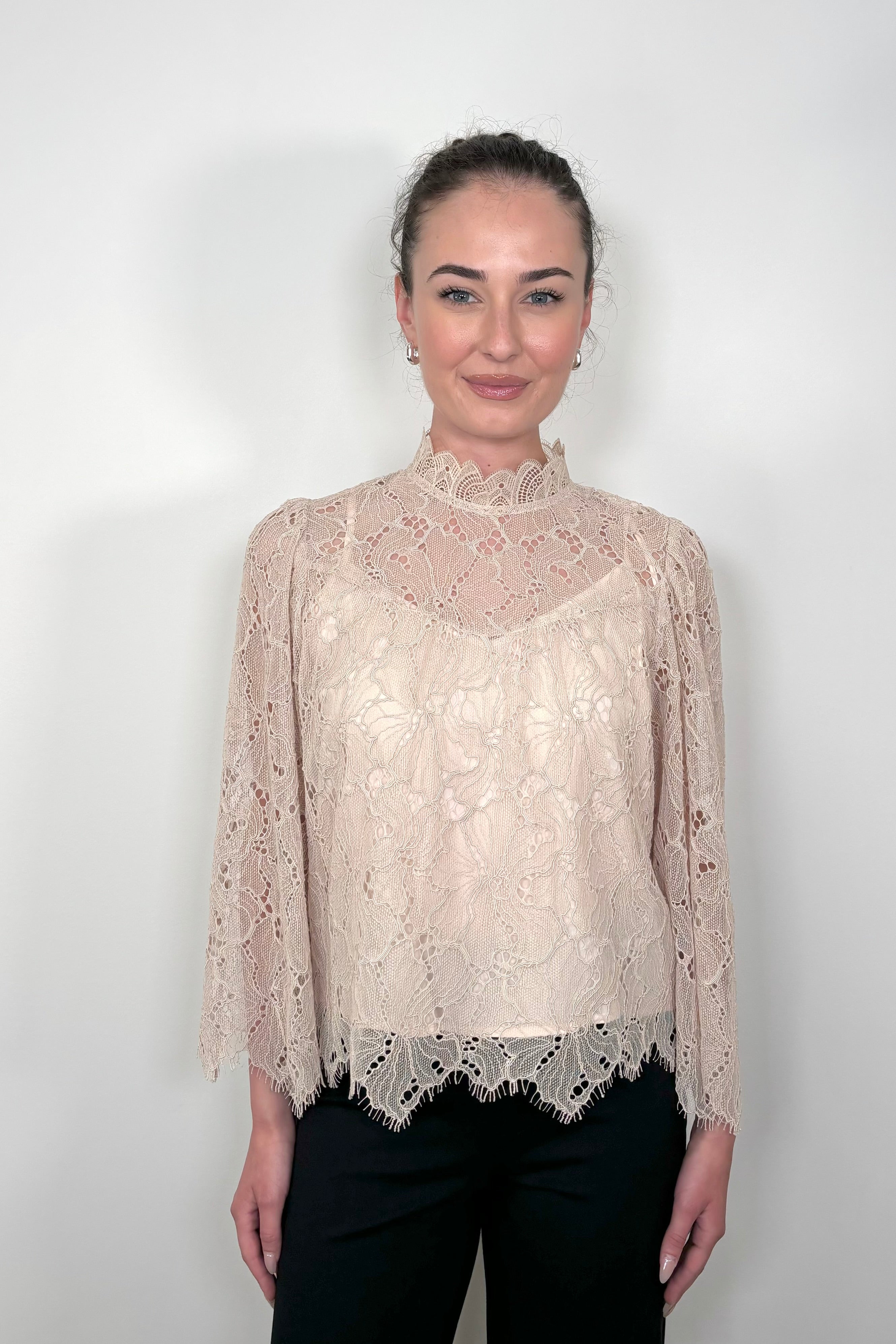 Front view of a woman wearing a lined long sleeve beige lace blouse 