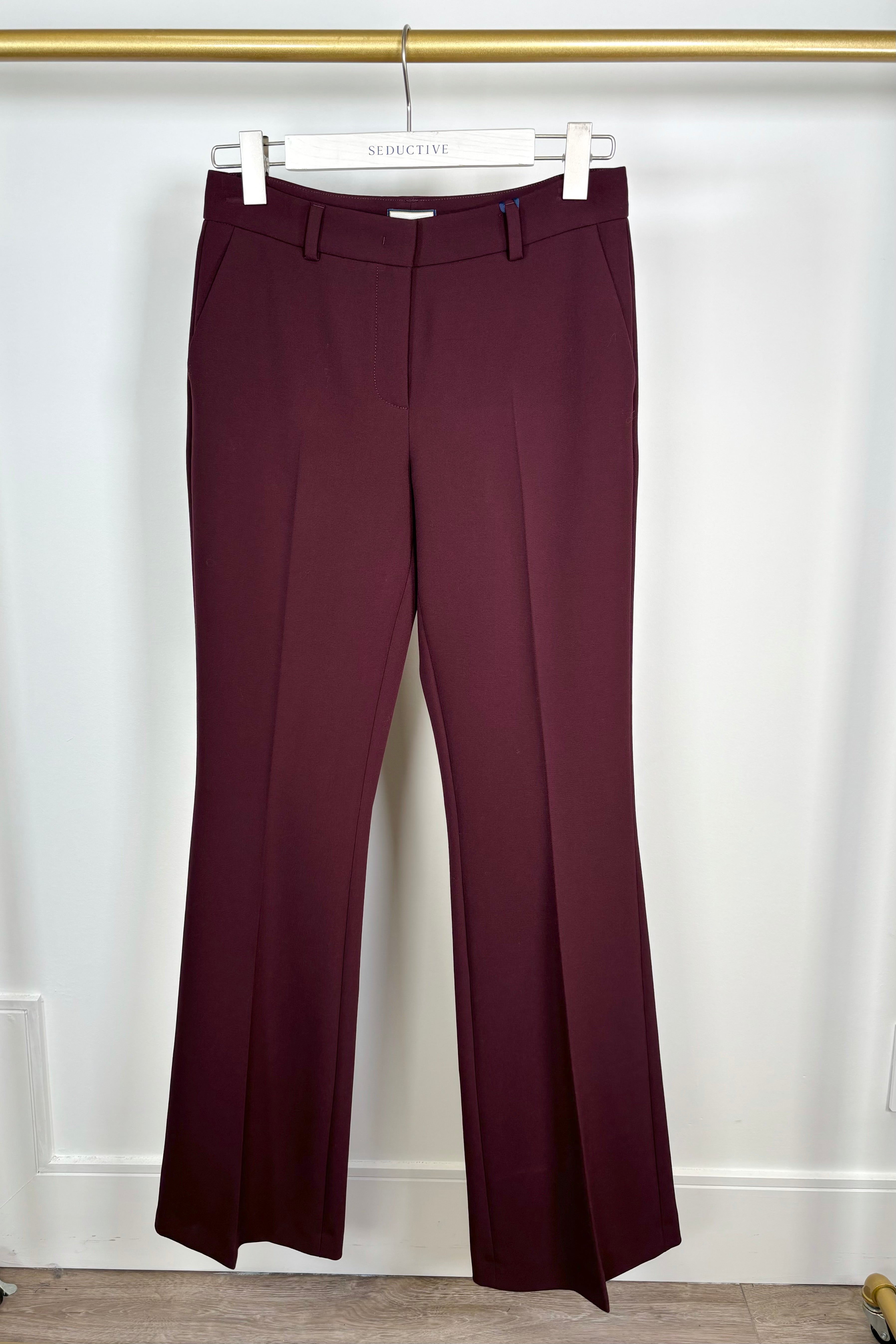 Maroon pants hanging on a white hanger against a white background