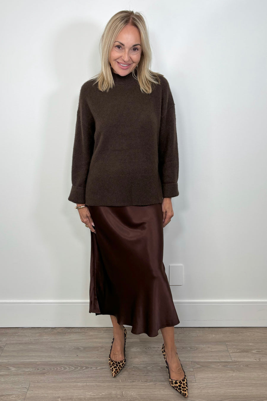Front view of woman wearing an oversized cashmere brown sweater paired with satin brown skirt