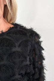 close-p of a person wearing a black top with sheer panels and frills
