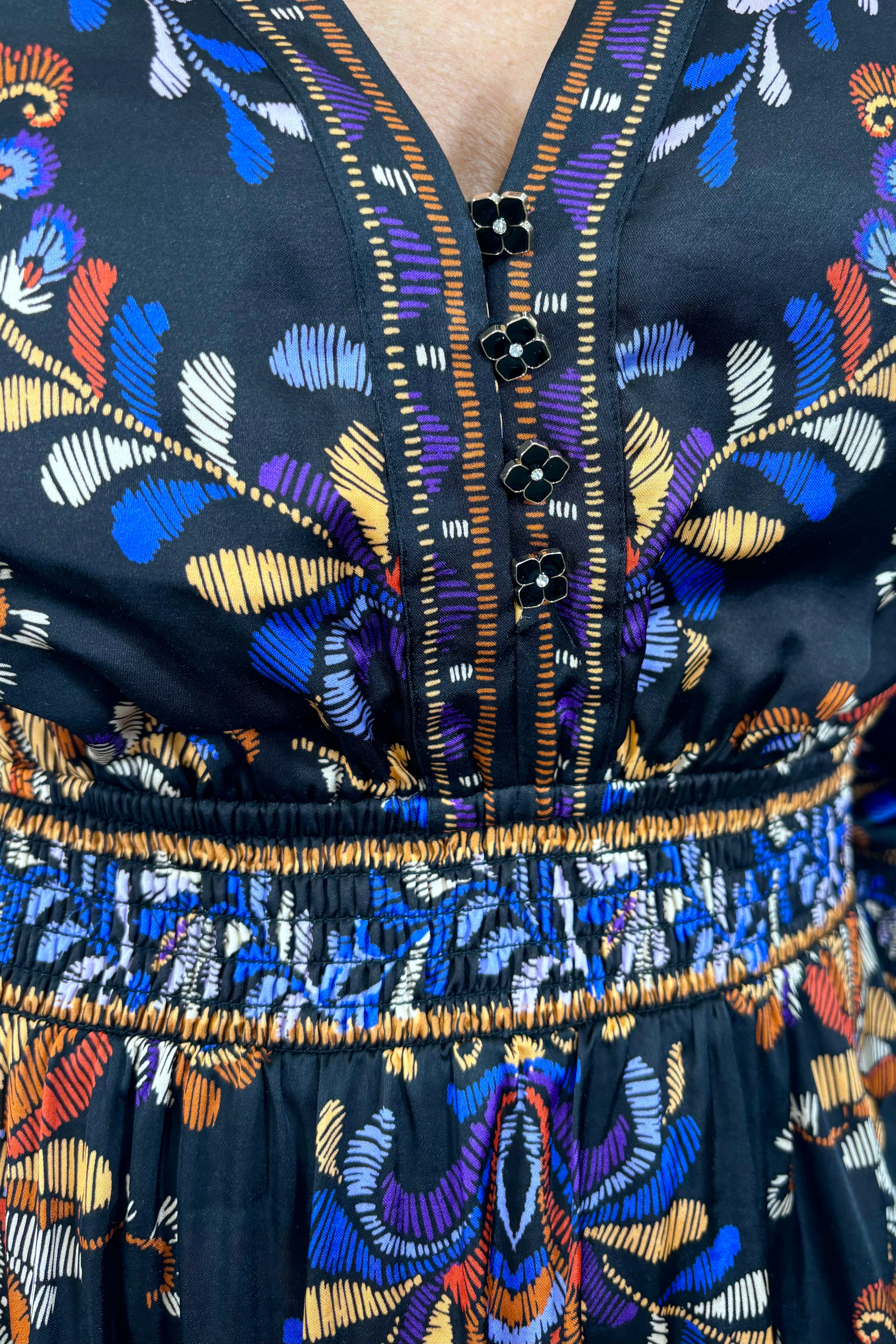 Close up view of woman wearing a satin black v-neck short long sleeve dress with a colourful pattern