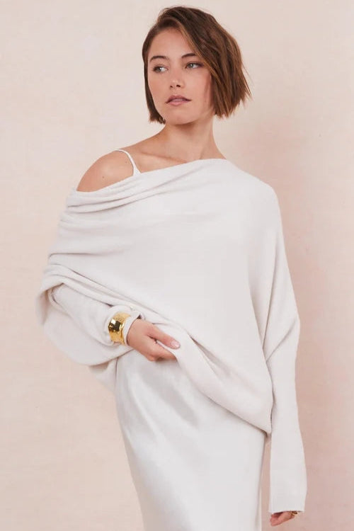 Woman wearing a white off-shoulder sweater against a beige background
