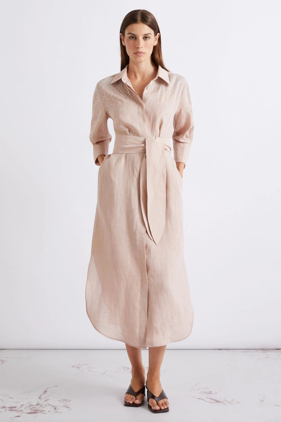 Woman wearing a blush pink collared midi dress with three-quarter sleeves, subtle embellishment, and a tie waist, front