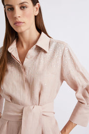 Woman wearing a blush pink collared midi dress with three-quarter sleeves, subtle embellishment, and a tie waist, detail
