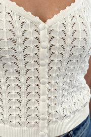 Close up of Woman wearing a cream knit camisole with buttons on the front, scalloped trim and open stitch detailing