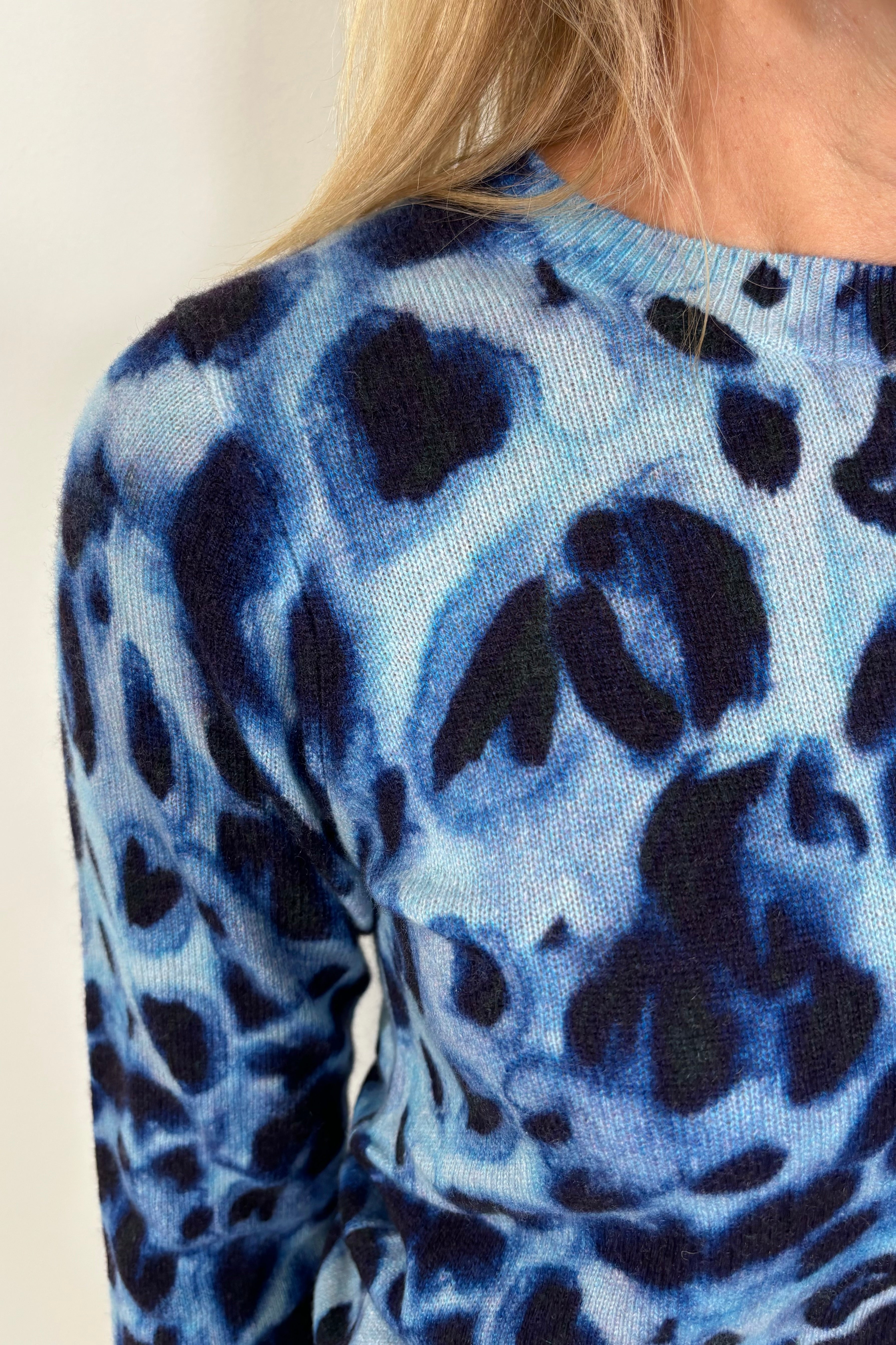 Zoom in of a woman’s right shoulder wearing a blue watercolour animal print 100% cashmere long sleeve sweater