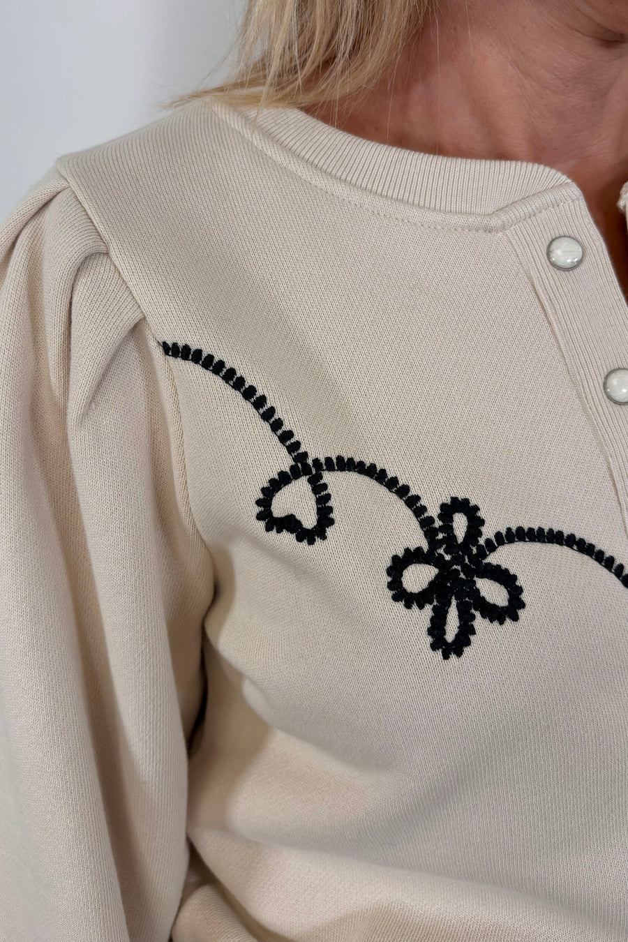 zoom in of a woman’s right shoulder wearing a ecru coloured sweatshirt with a western inspired detailing in the arms and chest