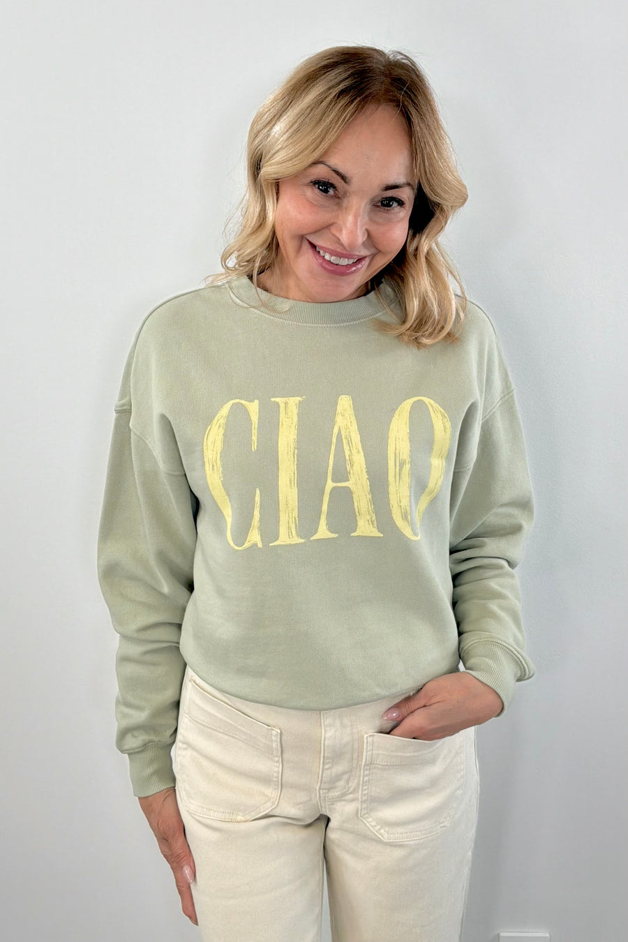 Woman wearing a matcha green pullover with " ciao " detail