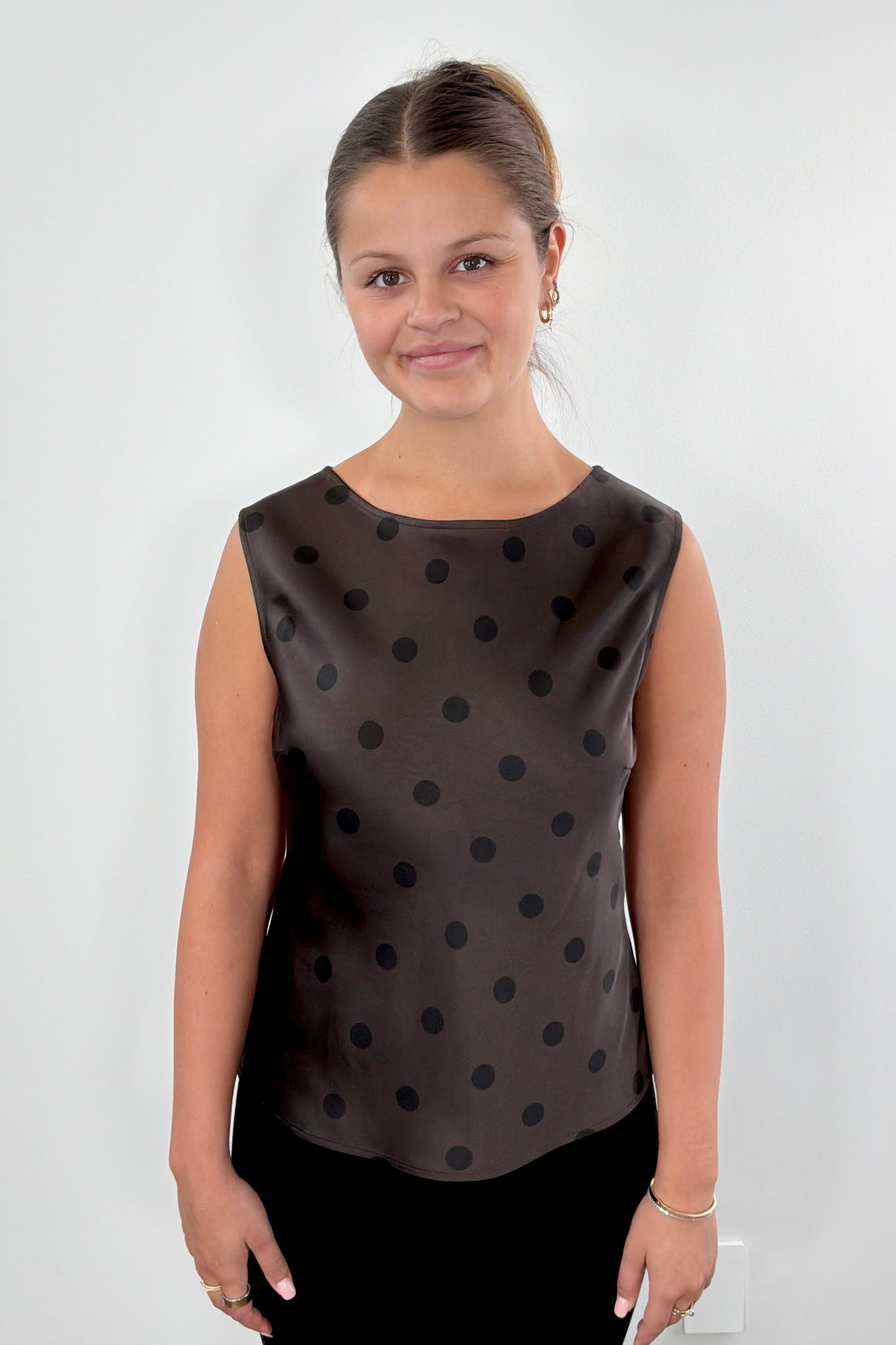 Woman wearing a brown sleeveless top with black polka dots