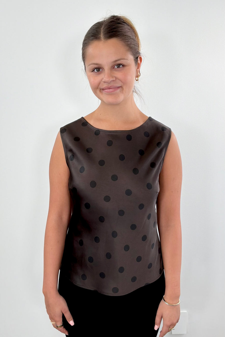 Woman wearing a brown sleeveless top with black polka dots