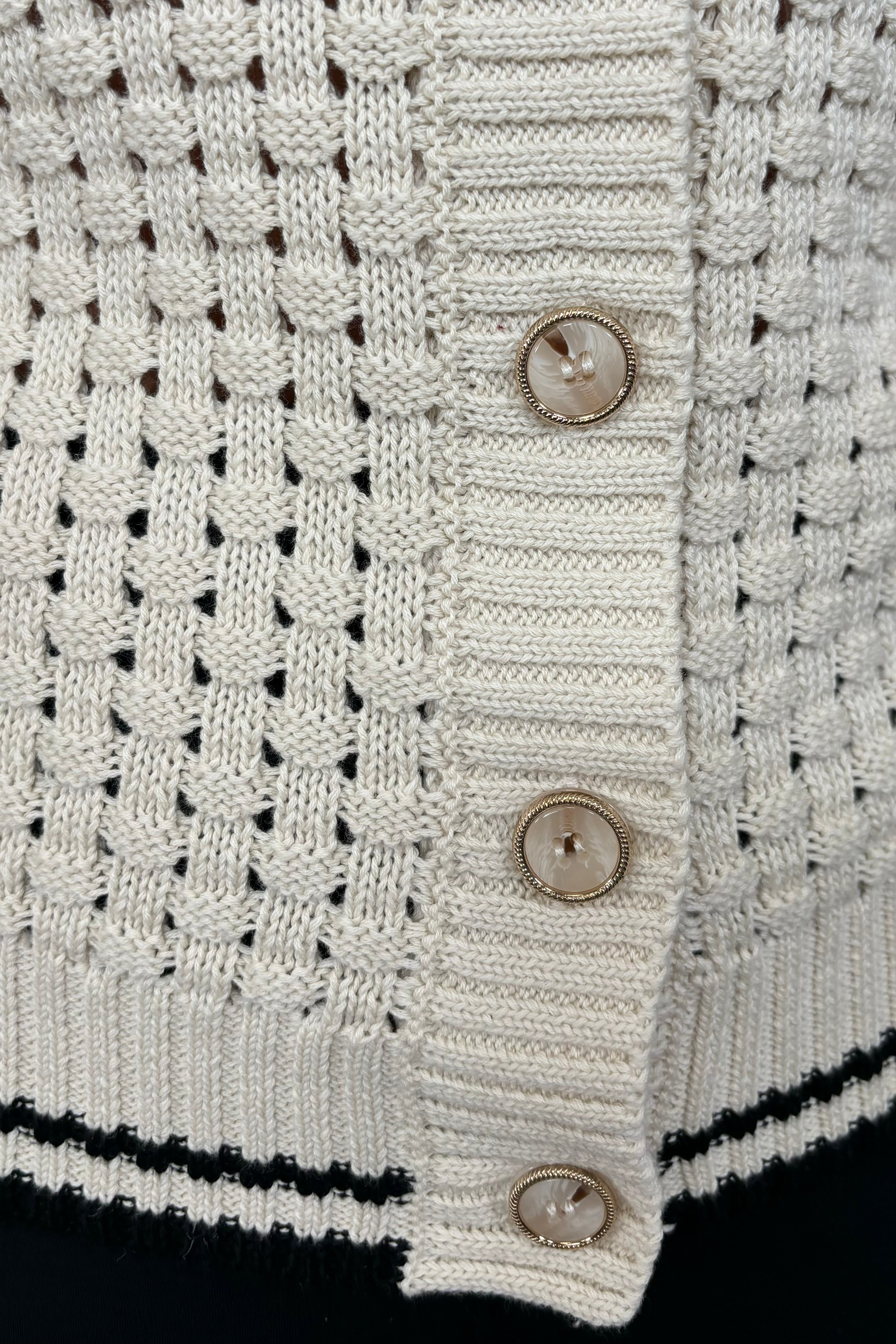Close-up of a woman wearing an off white melange knit cardigan with black trim 