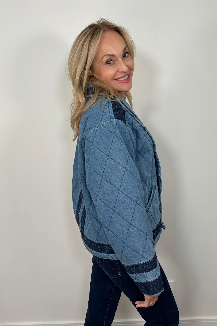 Side facing woman wearing a blue quilted jacket with navy blue detailing.