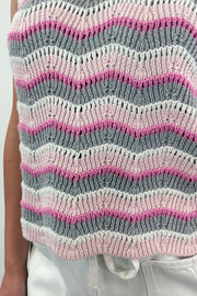 Close up of a woman wearing a knit vest in a zig zag stitch with a pink grey and white pattern
