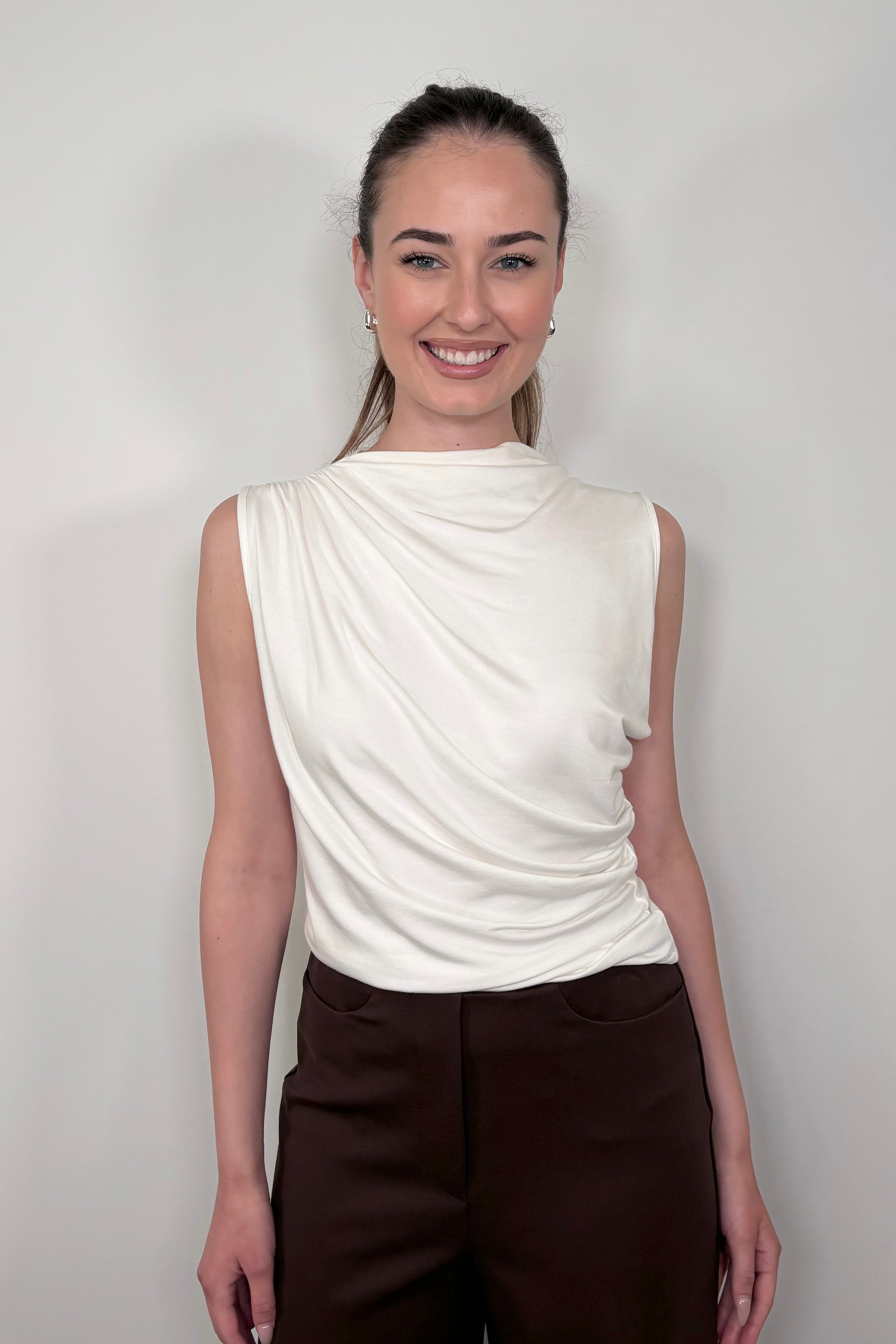 Front facing woman wearing a white rouched sleeveless top
