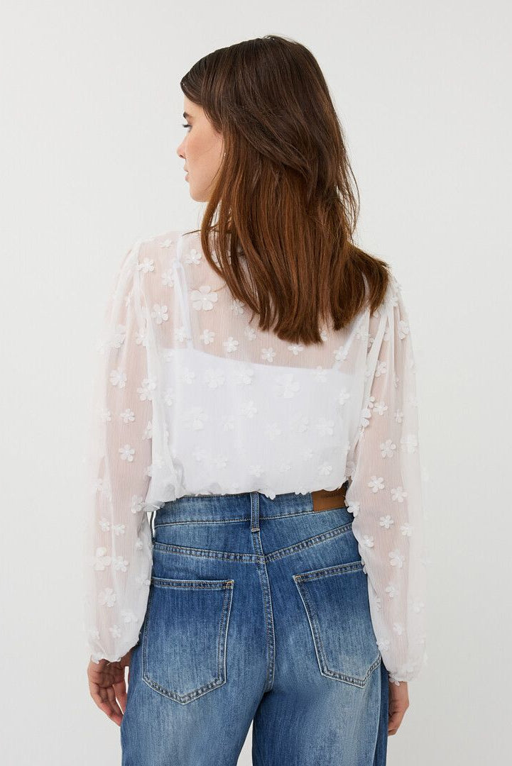 Woman wearing a sheer white long-sleeve blouse with floral texture, layered over a camisole, back view
