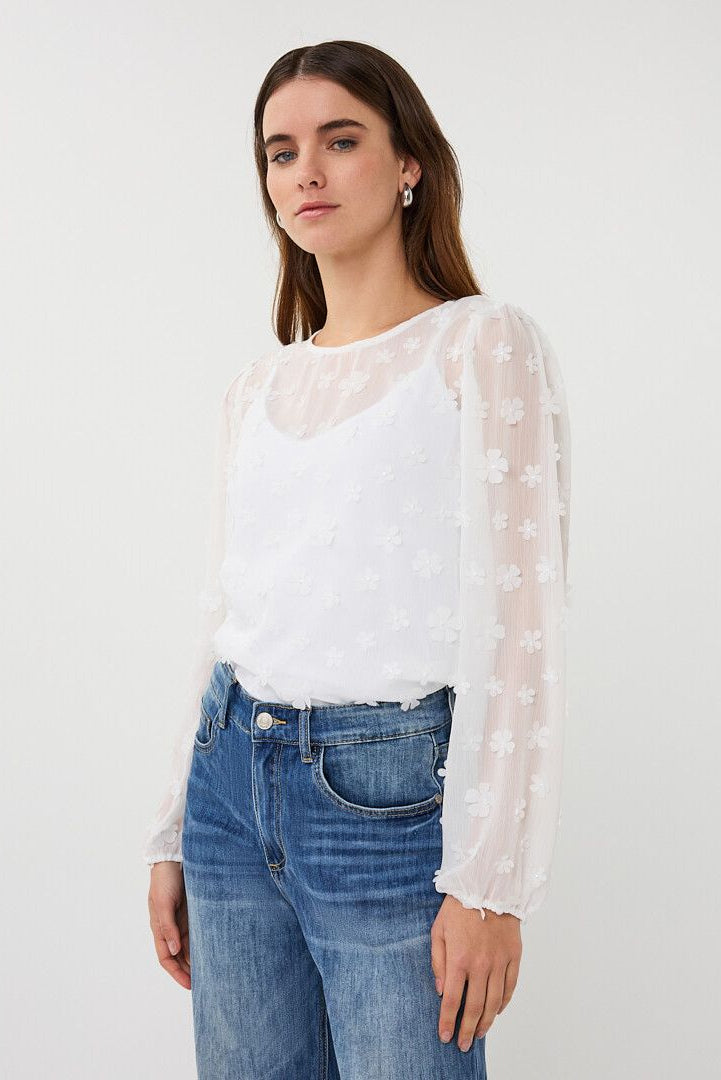 Woman wearing a sheer white long-sleeve blouse with floral texture, layered over a camisole, front view