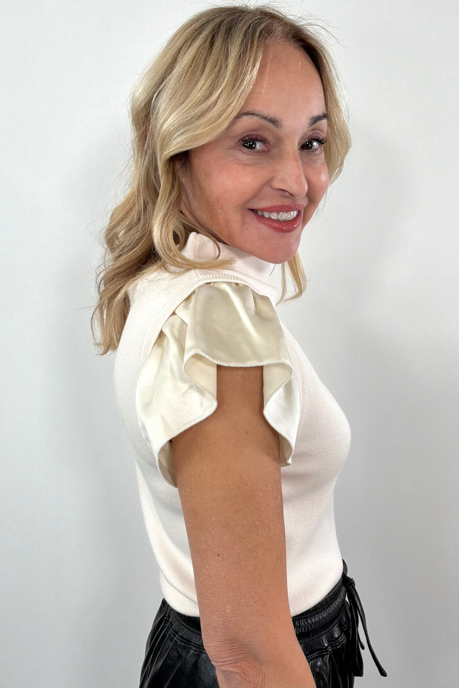 Woman wearing a white blouse with ruffled sleeves and black pants against a plain background