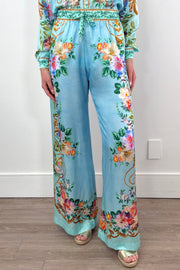 A woman wearing silk/viscose flowy pants in light blue with a floral pattern

