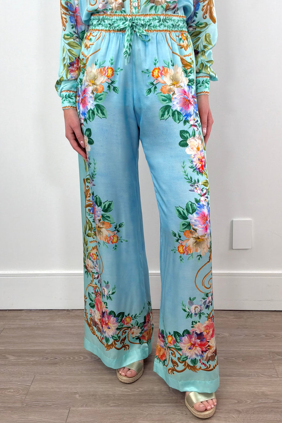 A woman wearing silk/viscose flowy pants in light blue with a floral pattern

