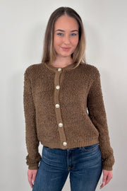 Woman wearing a brown knitted cardigan with white buttons against a plain background