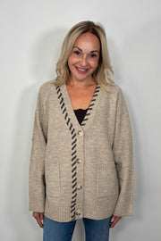 Front view of woman wearing a beige cardigan, v-neck and brown detailing