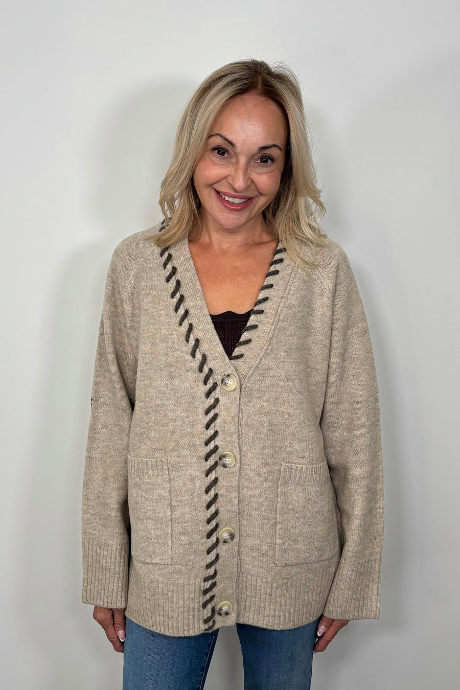 Front view of woman wearing a beige cardigan, v-neck and brown detailing