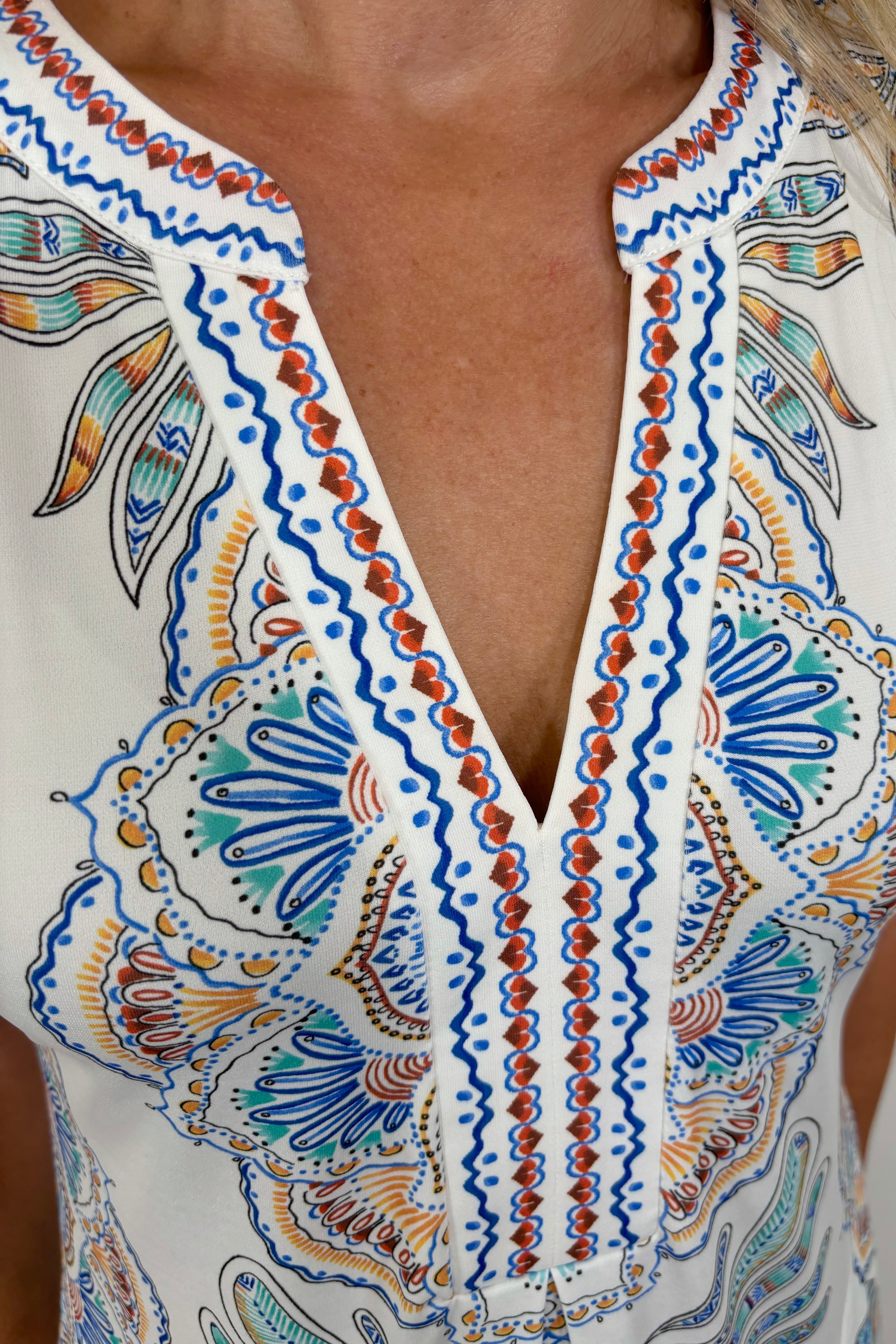zoom in to the neckline of a woman wearing a short white dress with blue, green, yellow and red detailing/pattern, short sleeved